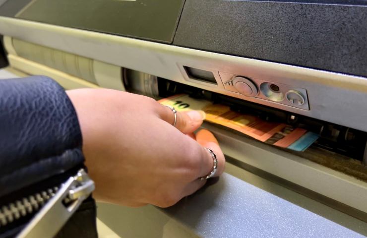 Mano che raccoglie soldi in euro da uno sportello ATM di una banca
